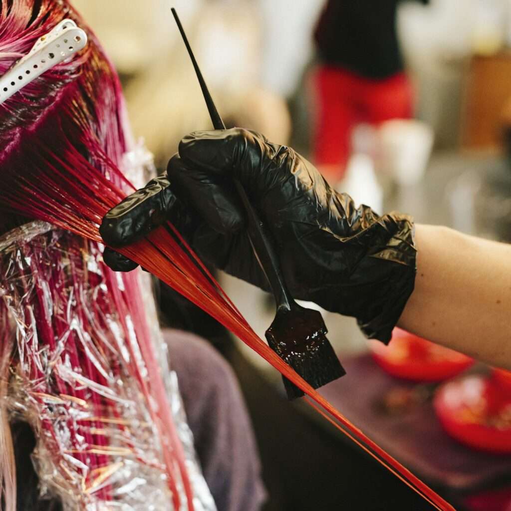 A hair colourist applying pink hair colour to a client's long blonde hair.