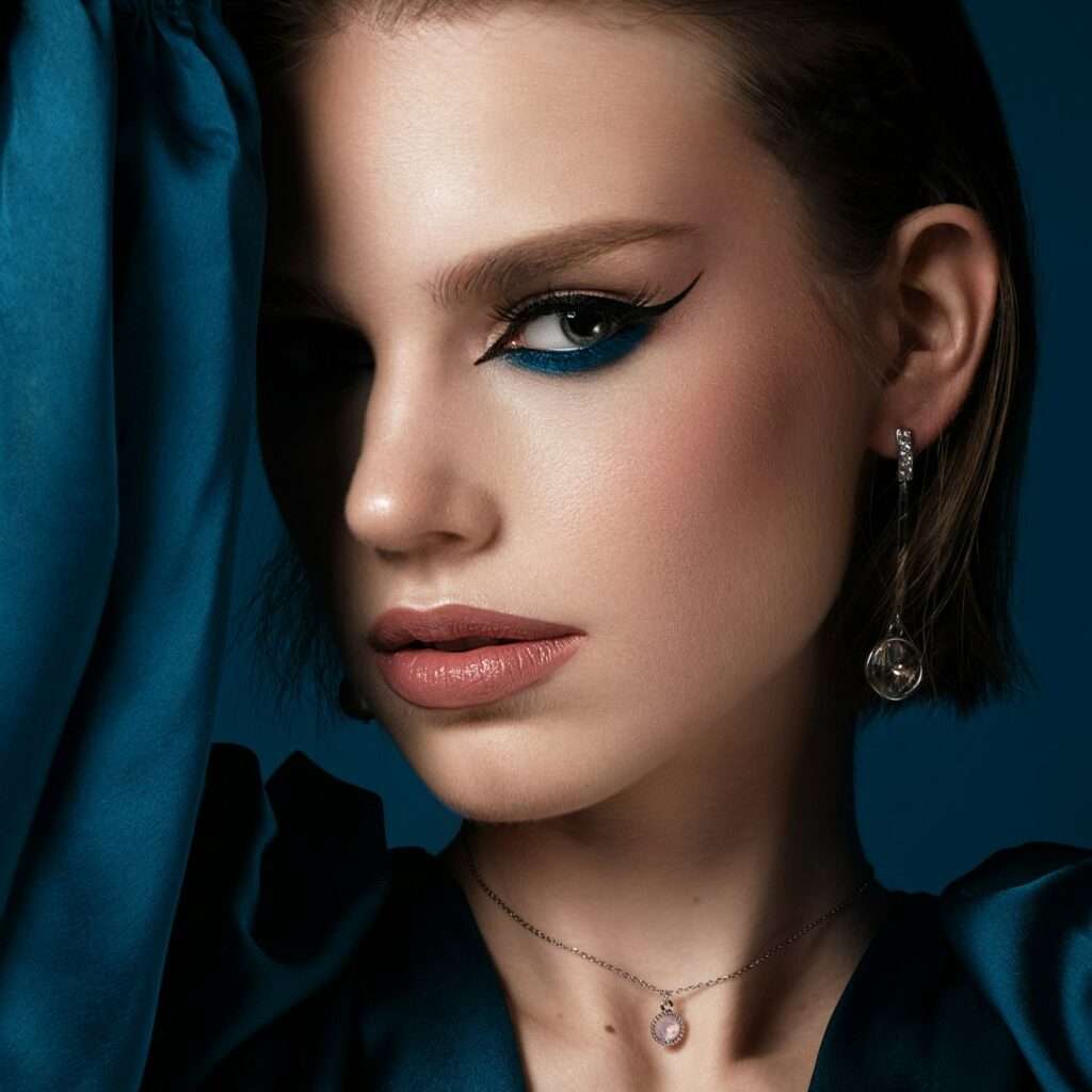 Beautiful woman with blue fabric and classic arrows art make-up. Beauty face.